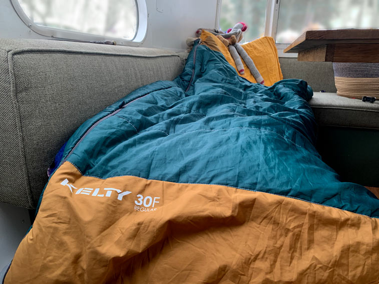 a teal and burnt orange sleeping bag strewn about an Airstream