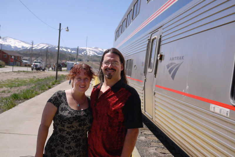 a couple stands in front of an Amtrak train
