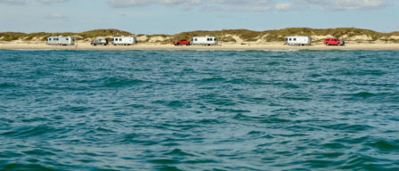 a view of the water, with a beach with RV camping in the distance