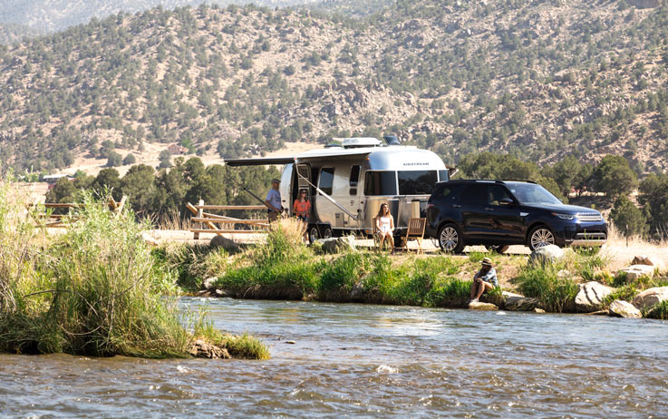an Airstream camped near a river in the desert mountains