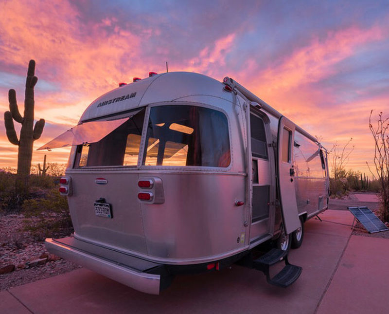 the lavendar and azul blanket of sunset repaints an Airstream travel trailer as it finds itself camping in the midst of a cactus forest in Twin Peaks Campground, Organ Pipe Cactus National Monument