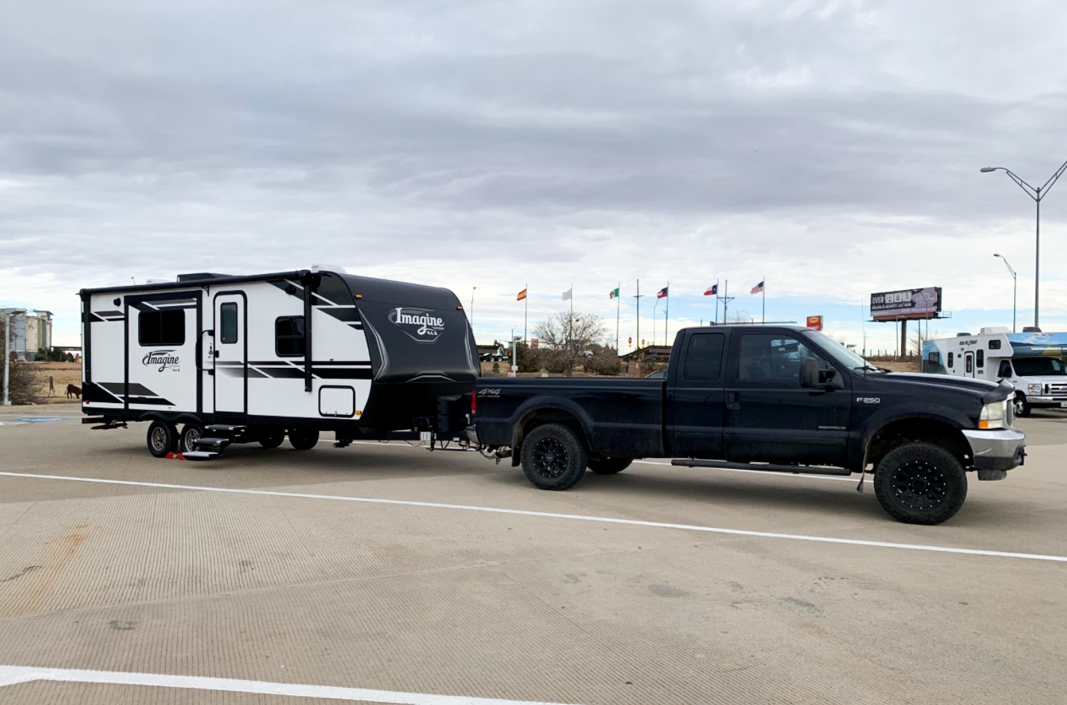 Black truck towing a travel trailer parked at a rest stop.