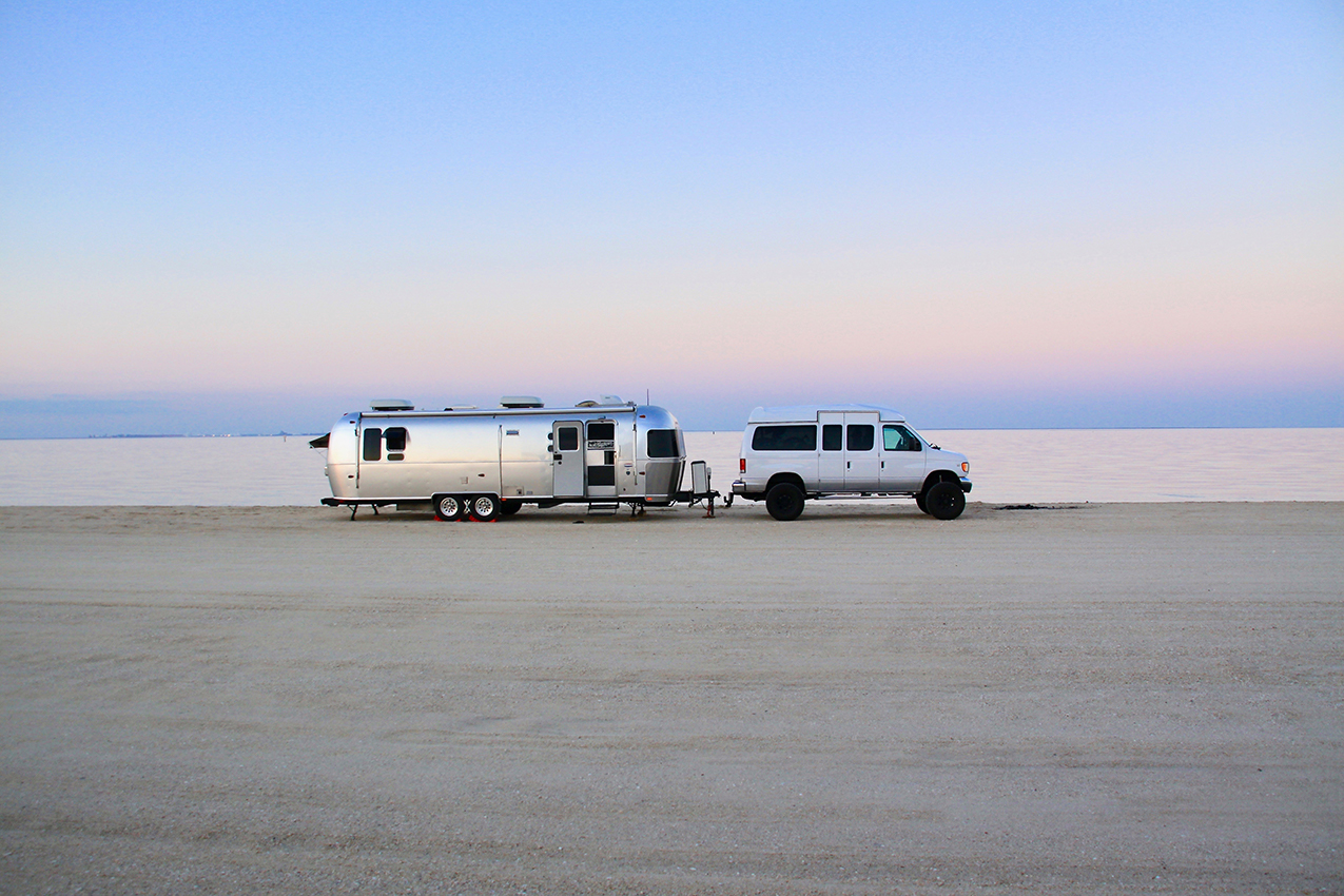 Van with Airstream on beach at sunset