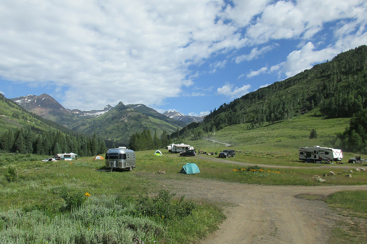 Several RVs parked in field with mountains