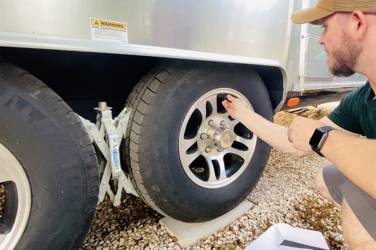 Person kneeling in front of RV tires with a chock between them.