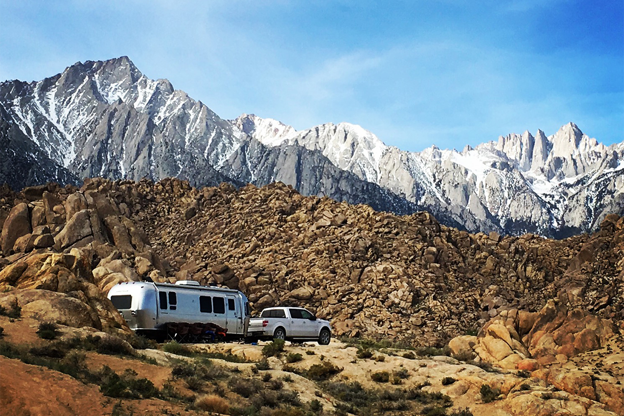 RV parked amongst rocks and white cap mountains.