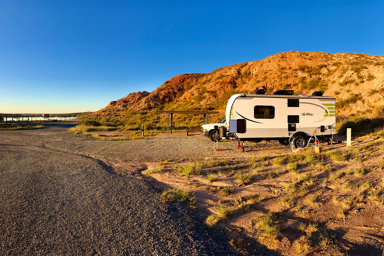 RV parked in front of hill near a lake at sunset