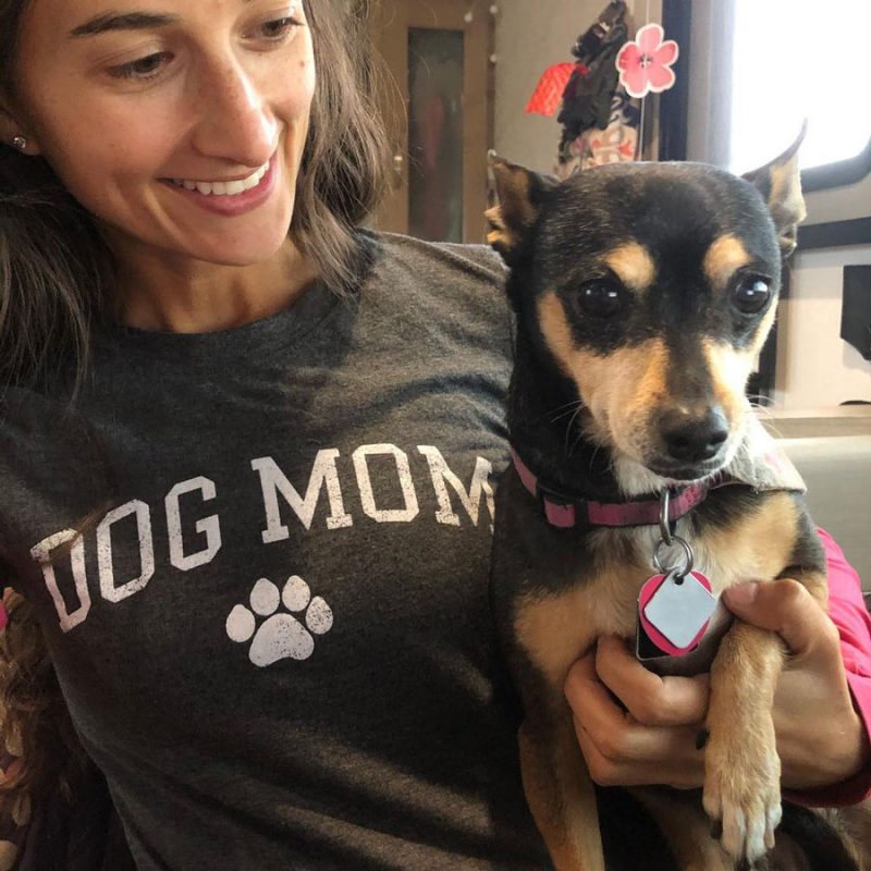 a woman wearing a shirt that says dog mom while holding her dog.