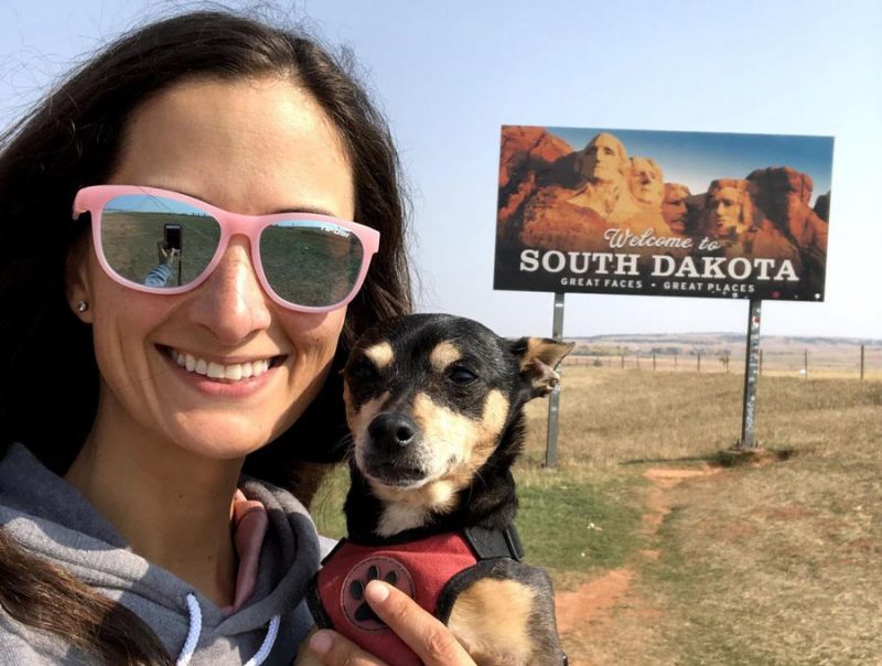 a woman and her dog pose near the South Dakota welcome sign