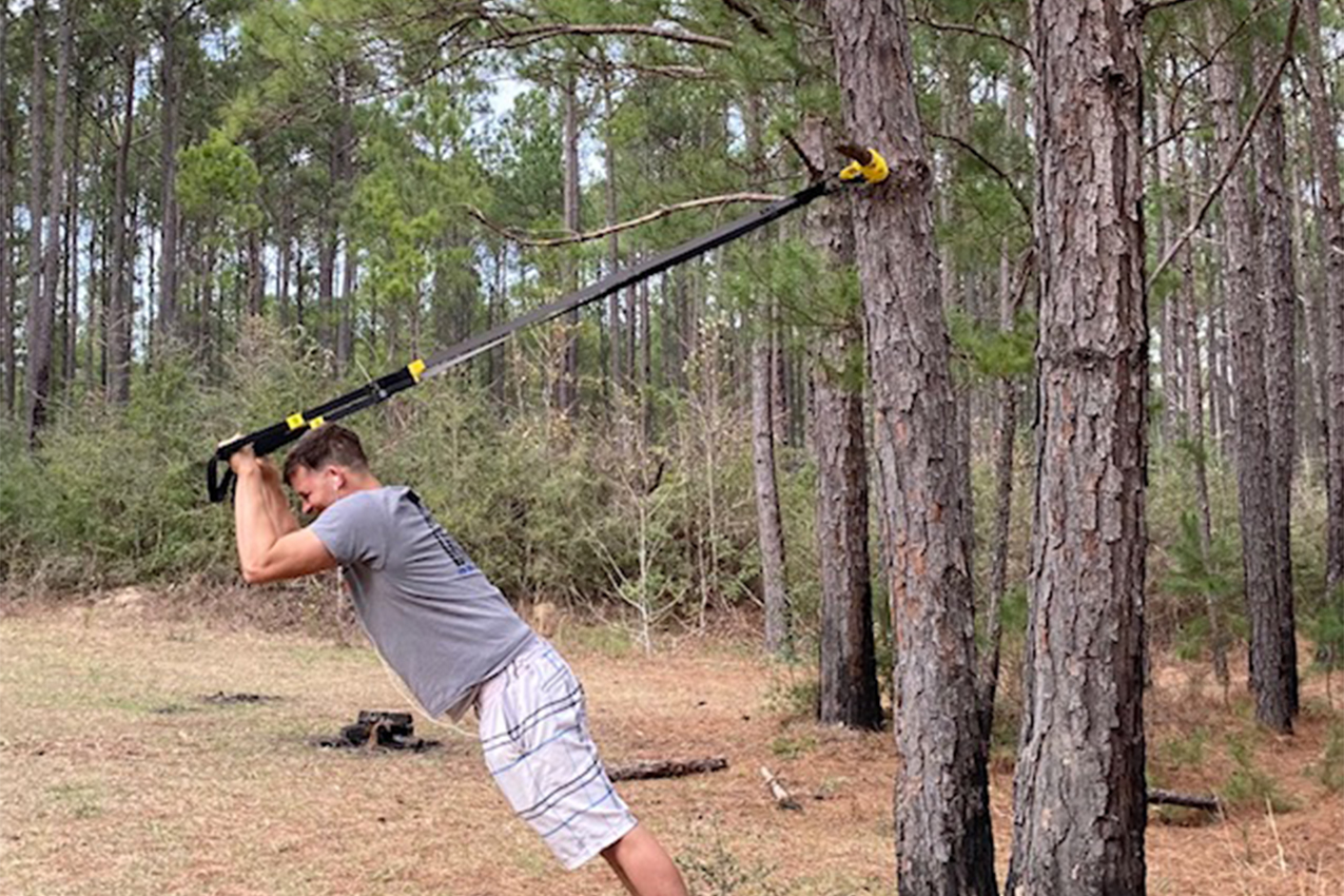 Man using TRX to work out in the forest.