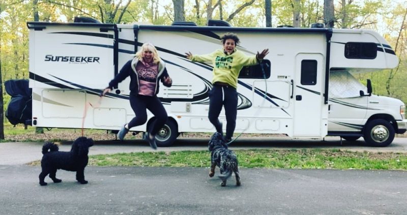 a mom and her son jump up in the air simultaneously in front of their RV