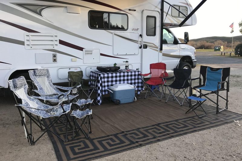 Chairs and a table and a mat set up outside of an RV