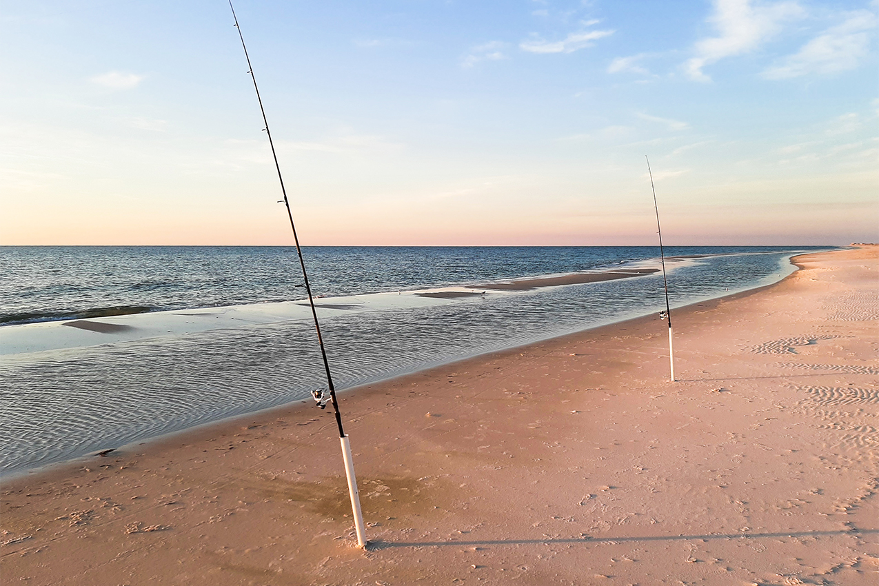Two fishing poles in the ocean at sunset