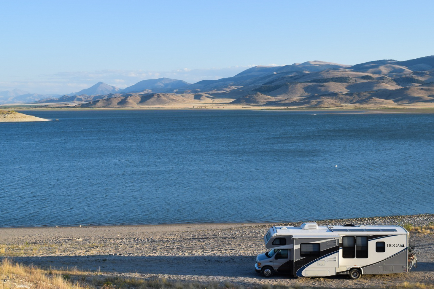 RV parked in front of a blue lake with mountains in the background