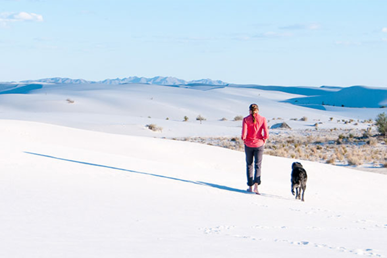 Woman on sand dunes with her dog.
