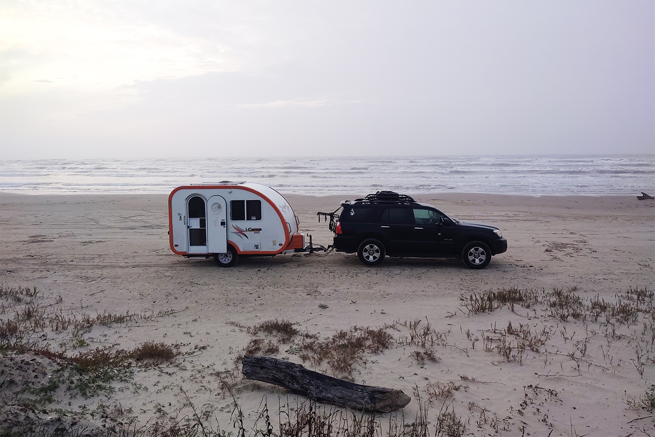 Teardrop camper and tow vehicle parked on the beach.