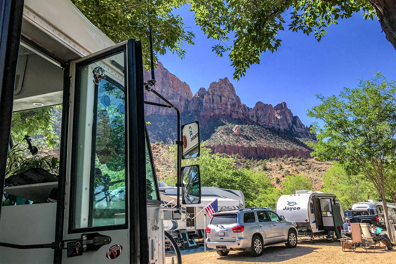 Bus with several RVs in the background parked in Zion National Park.