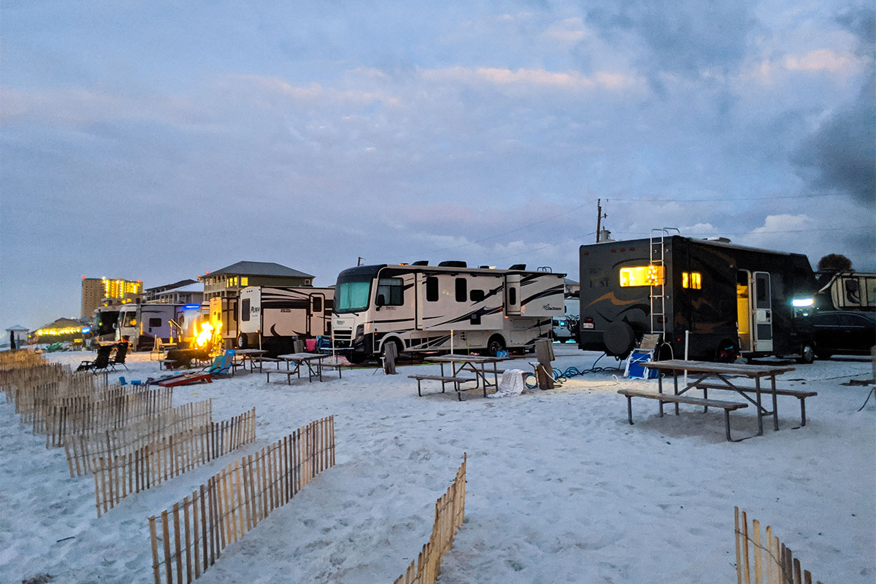 Several RVs parked on a beach at dusk.