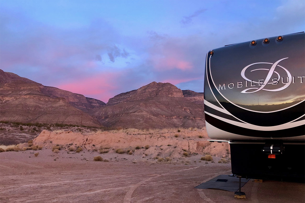 Fifth wheel parked in the desert during sunset.