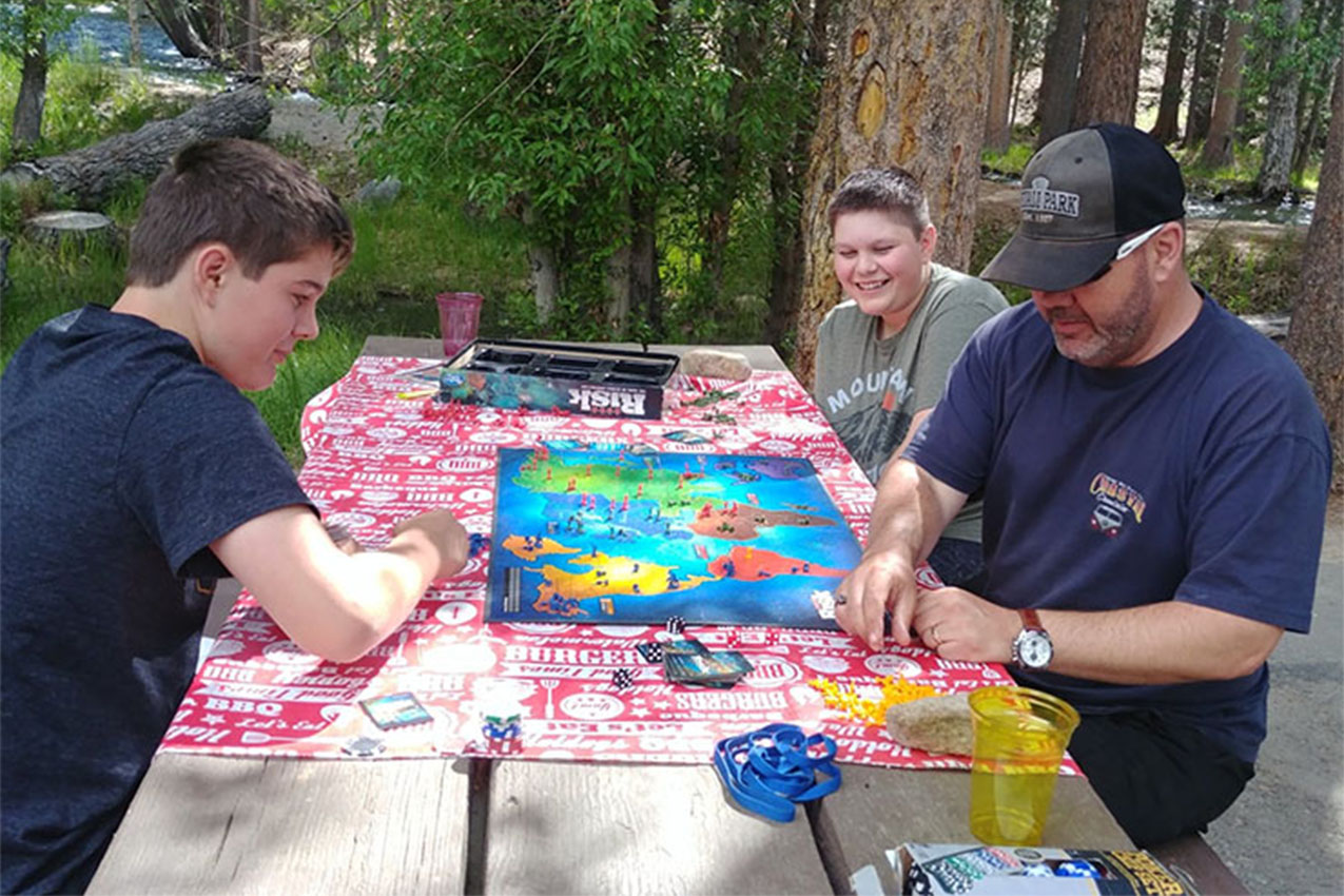 Family sitting at picnic table playing a game of Risk.