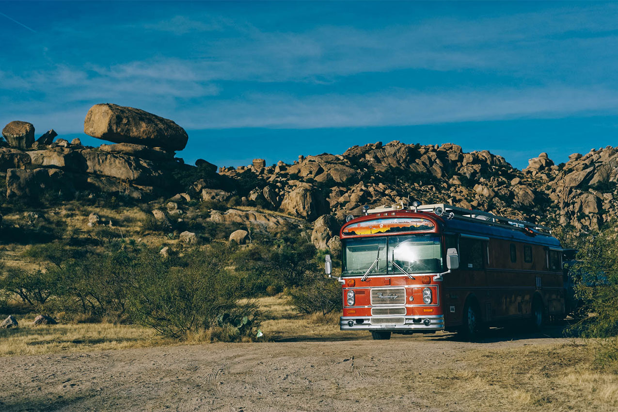 Red bus parked in front of bread shaped rocks.