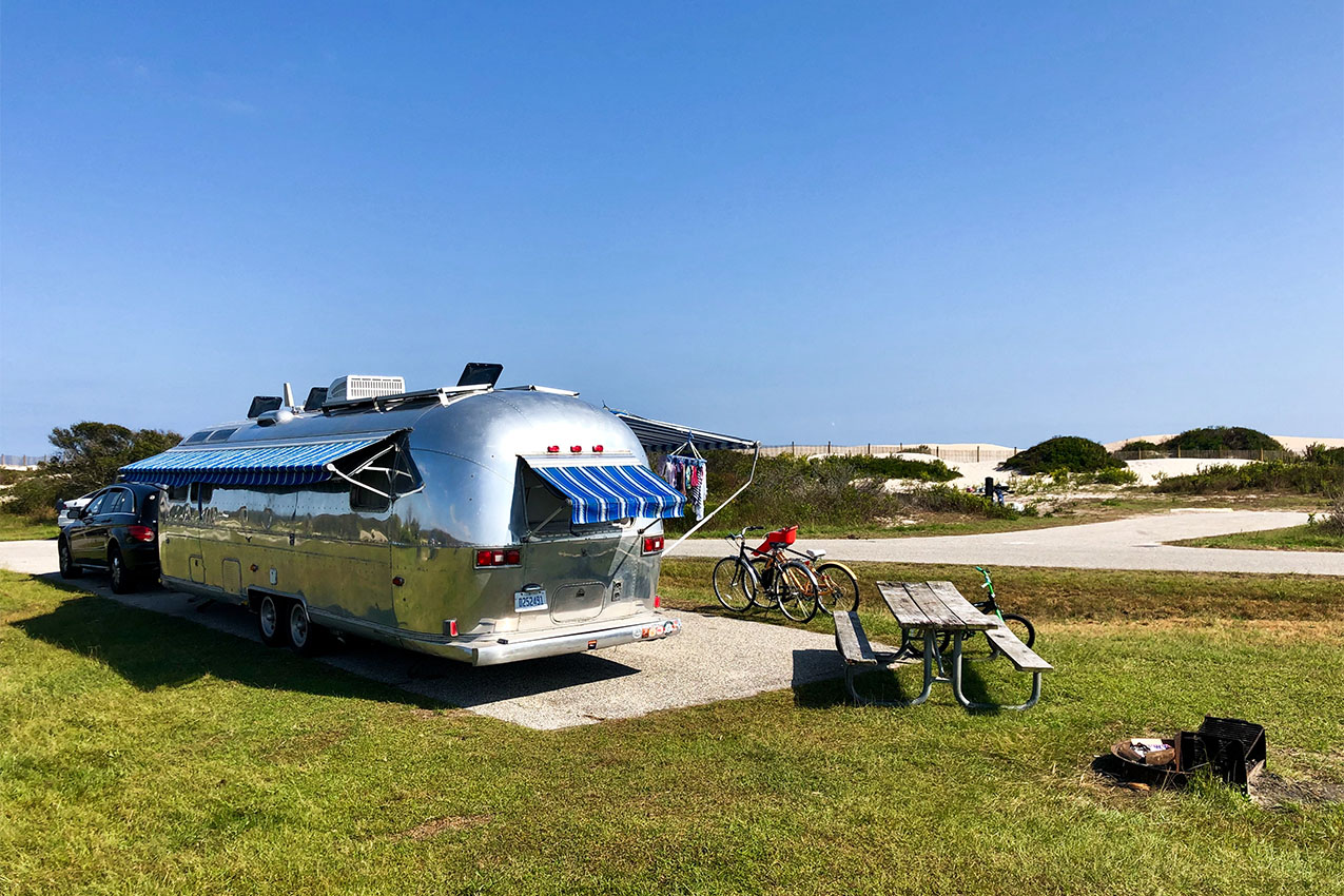 Airstream with bikes out parked near sand dunes at the beach.