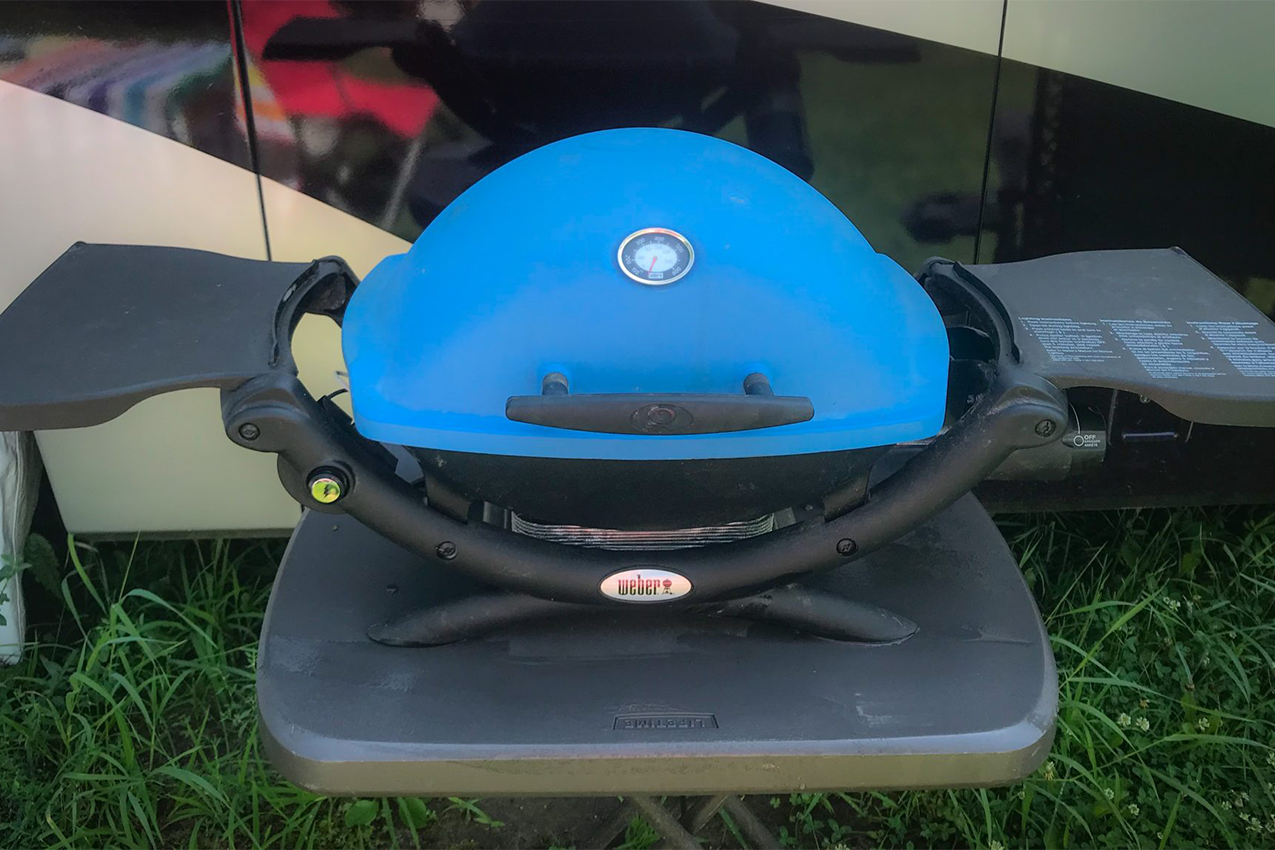 Blue portable grill set up outside an RV.