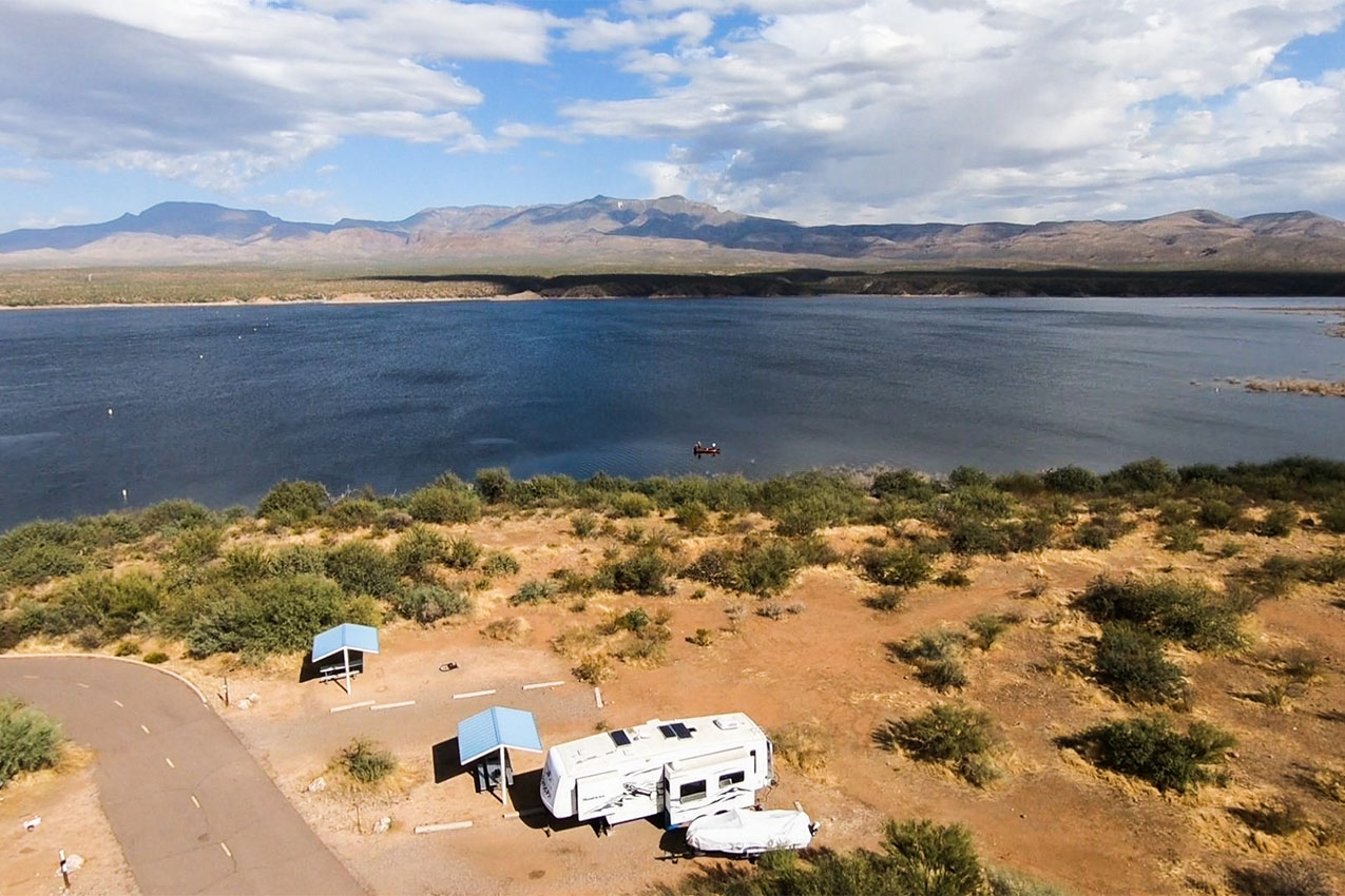 Aerial view of fifth wheel and boat parked in a campsite near a lake.