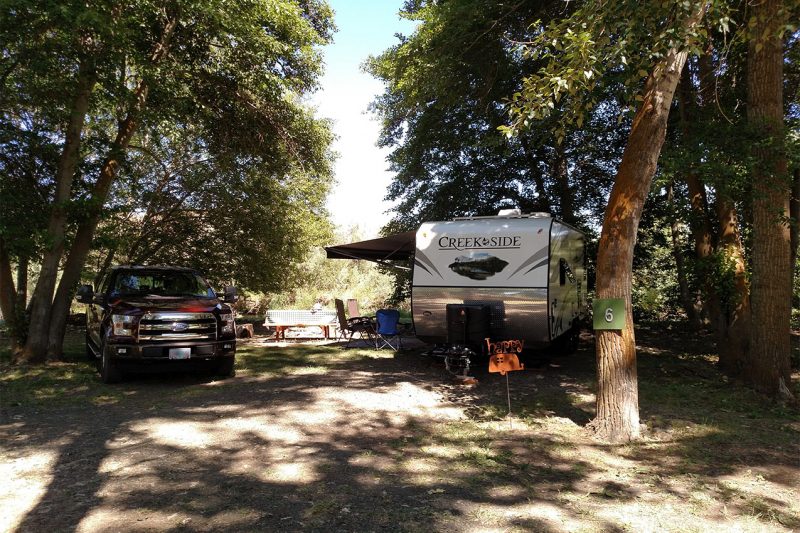 RV campsite with RV and car parked in the shade.