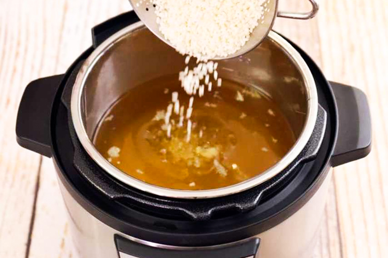 Pouring rice into Instant Pot filled with soup.