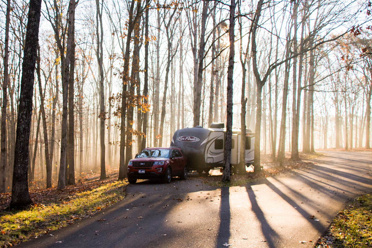 Truck and travel trailer parked in the woods with light streaming through the trees.