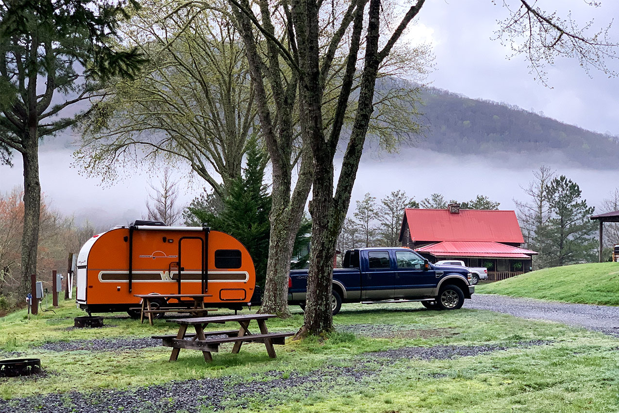 Orange teardrop trailer parked in front of mountains with low clouds.