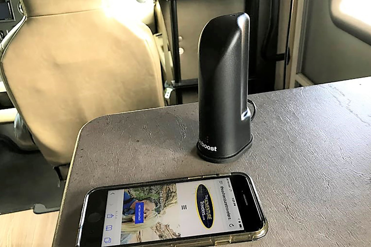 A black cell signal booster on an RV countertop next to a cell phone.