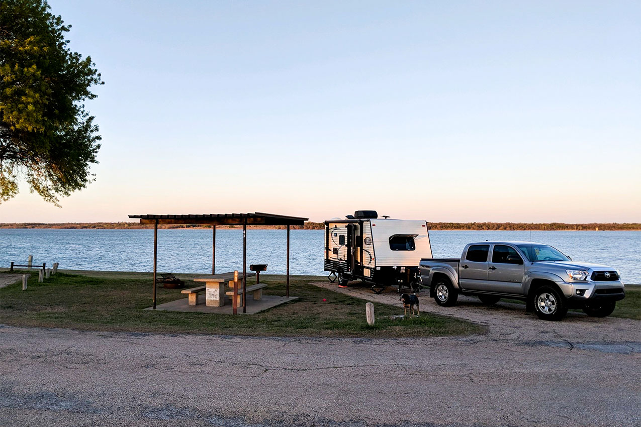 Truck and RV parked next to a lake and a covered picnic table.
