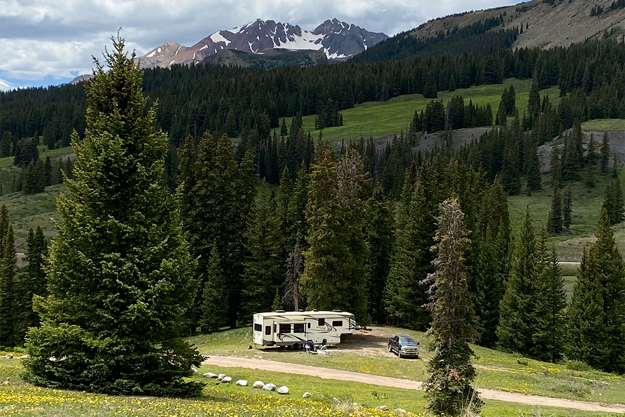 Truck and fifth wheel surrounded by evergreen trees and green hills.