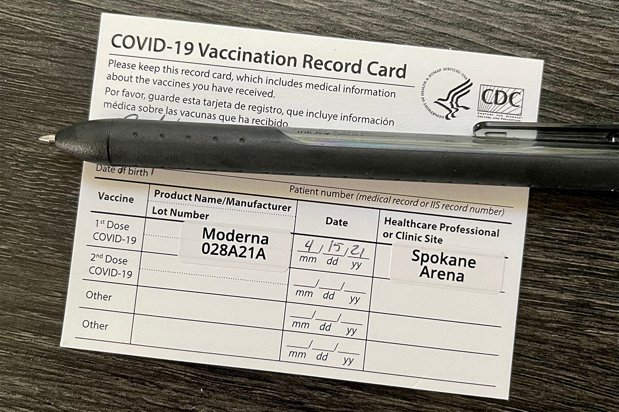 COVID-19 vaccination card on table with pen covering personal information.