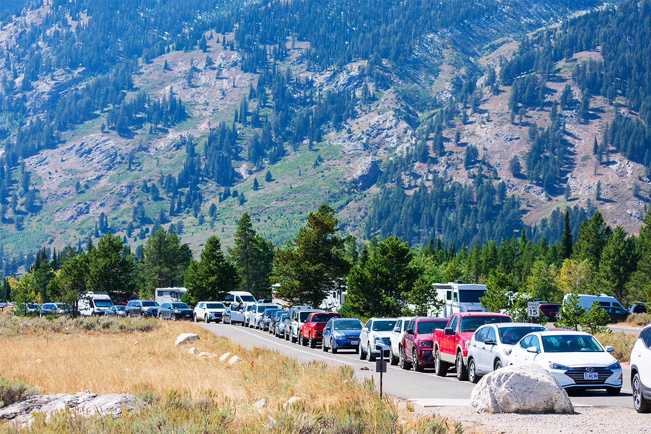 Long line of cars outside a national park with mountains in the background.