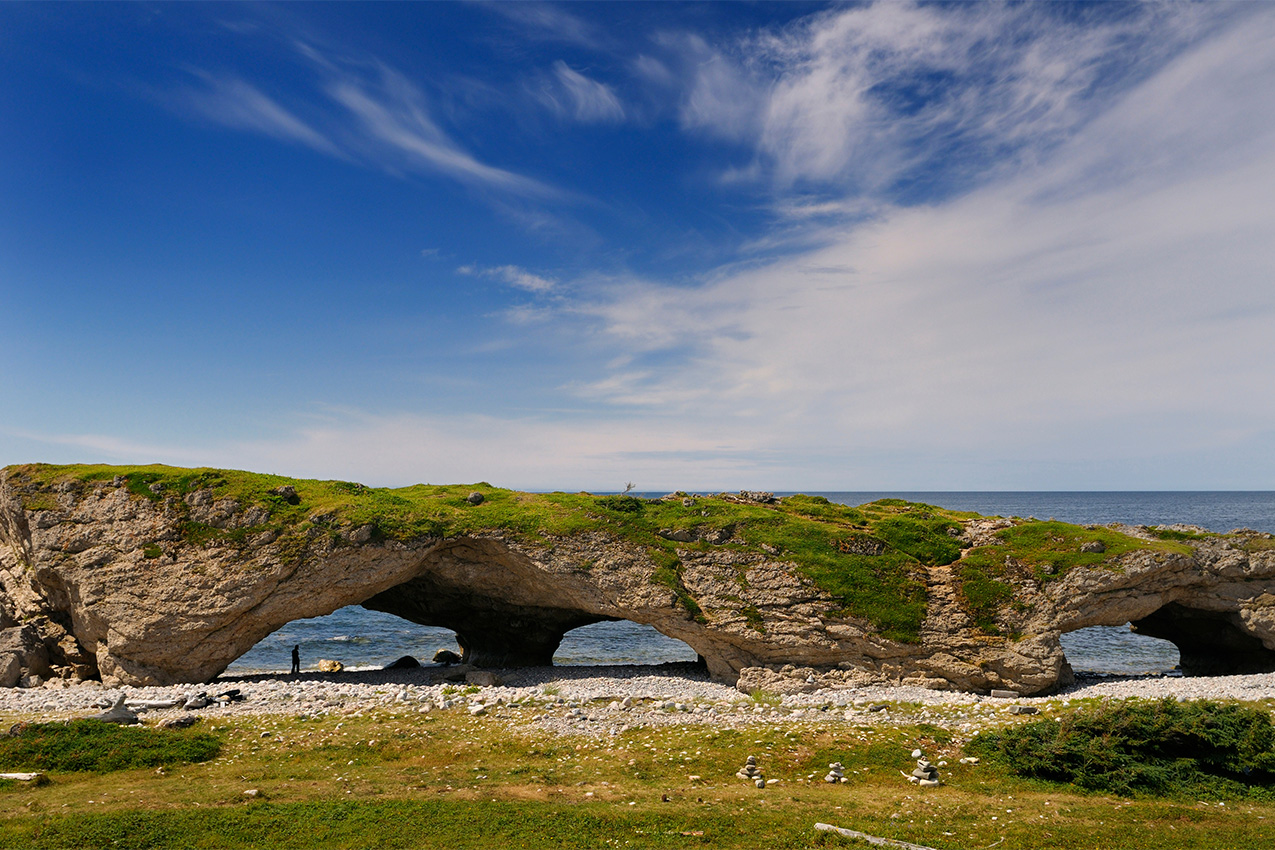 Grass covered rock arch on a shoreline.