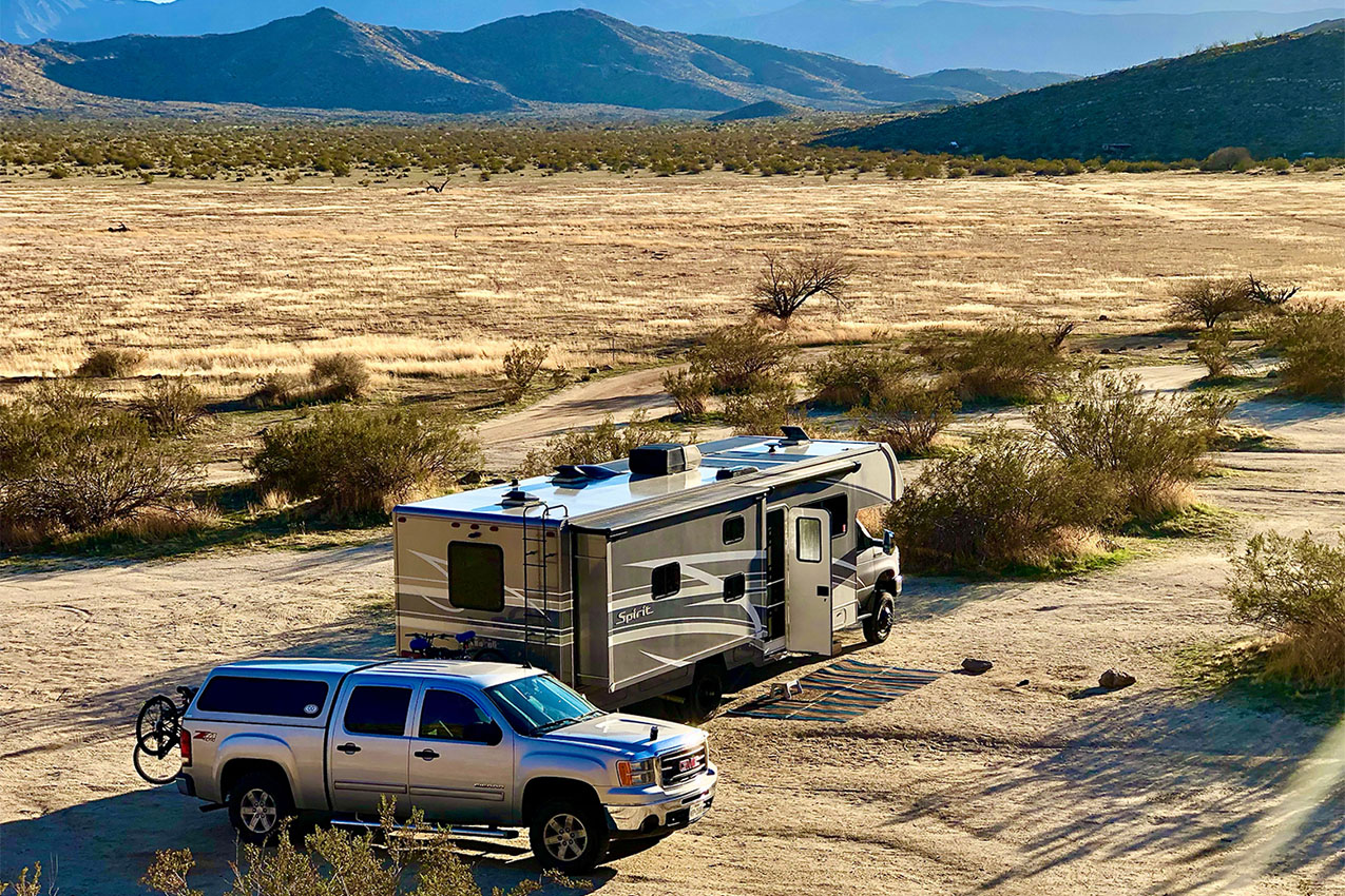 Truck and class C RV parked in the open desert.