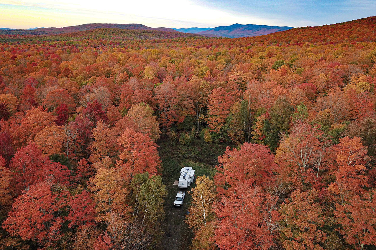 Drone photo of RV tucked in the forest covered with red and orange fall colors.