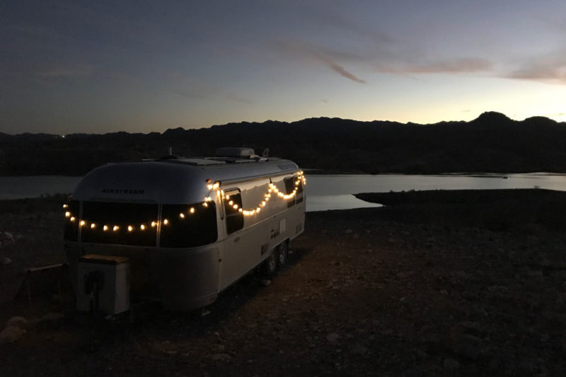 An Airstream decorated with Christmas lights camping next to a lake