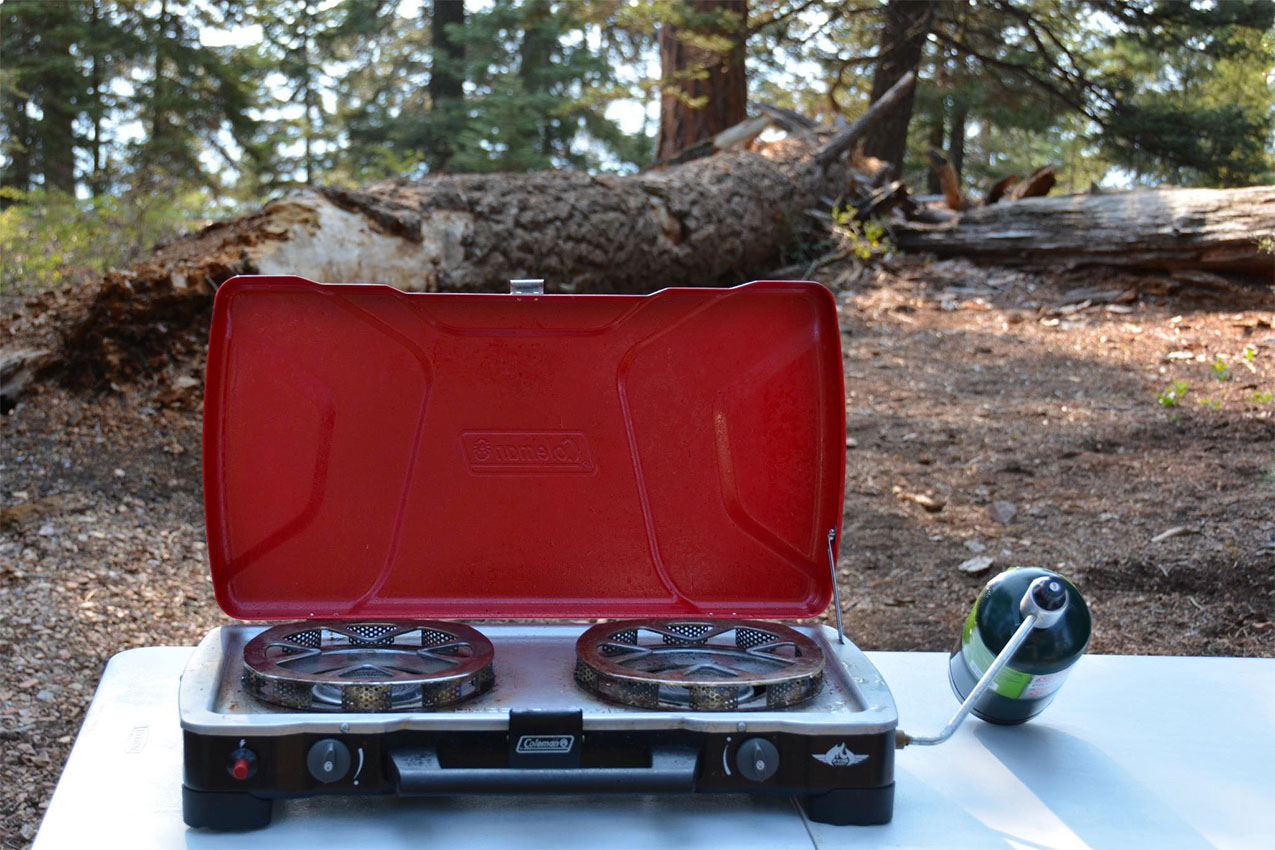 A camp stove with the lid open on a table outside.