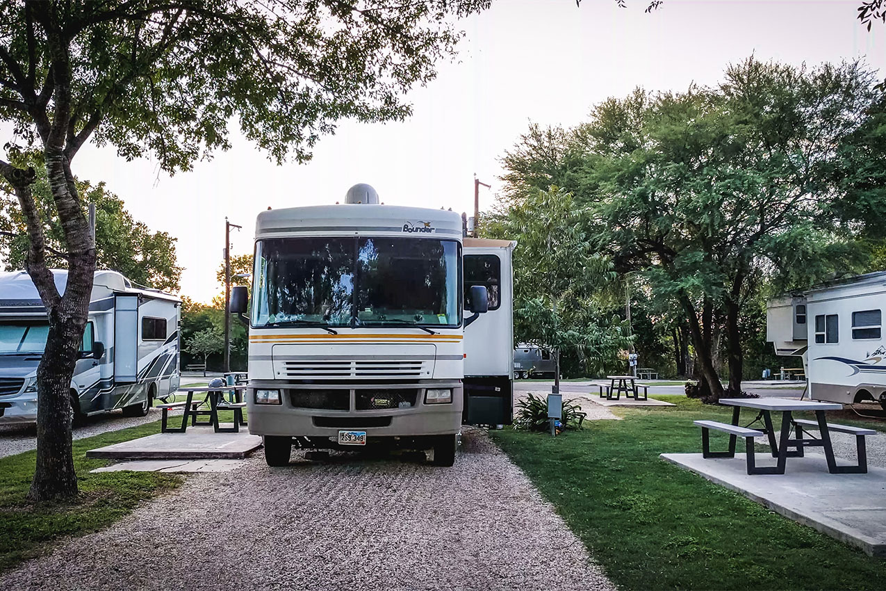 White class A parked in a gravel site at an RV park next to a picnic table.