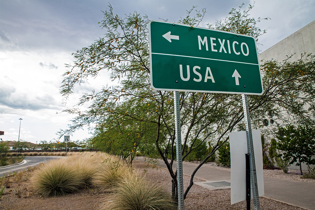 Green directional sign with white arrow point left for Mexico and arrow pointing up for US.