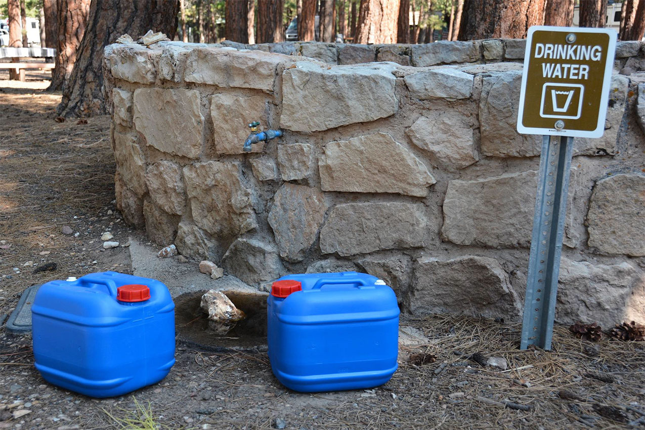 Two blue plastic water jugs next to a spigot.