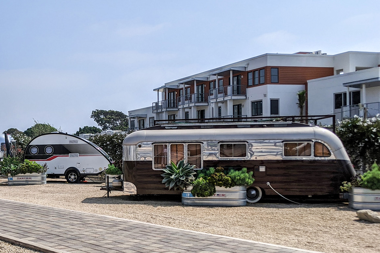 Small teardrop camper and vintage metal and wood RV parked in front of apartments.