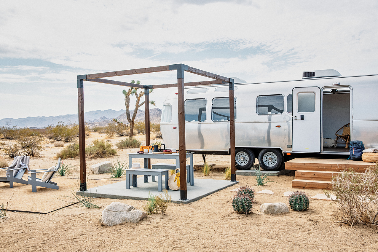 Airstream parked in the desert by an open cabana and Adirondack chairs.