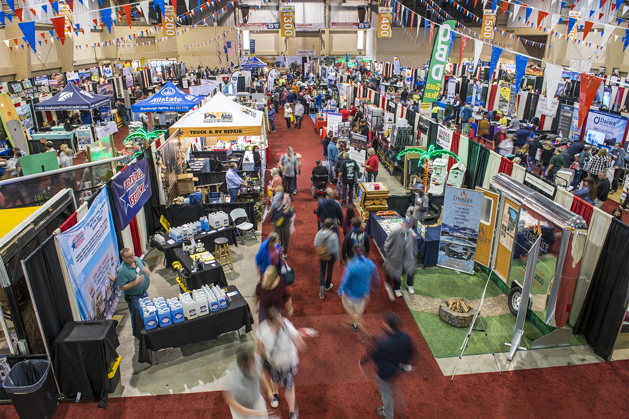 View from above of indoor RV show with vendors set up and people walking around.