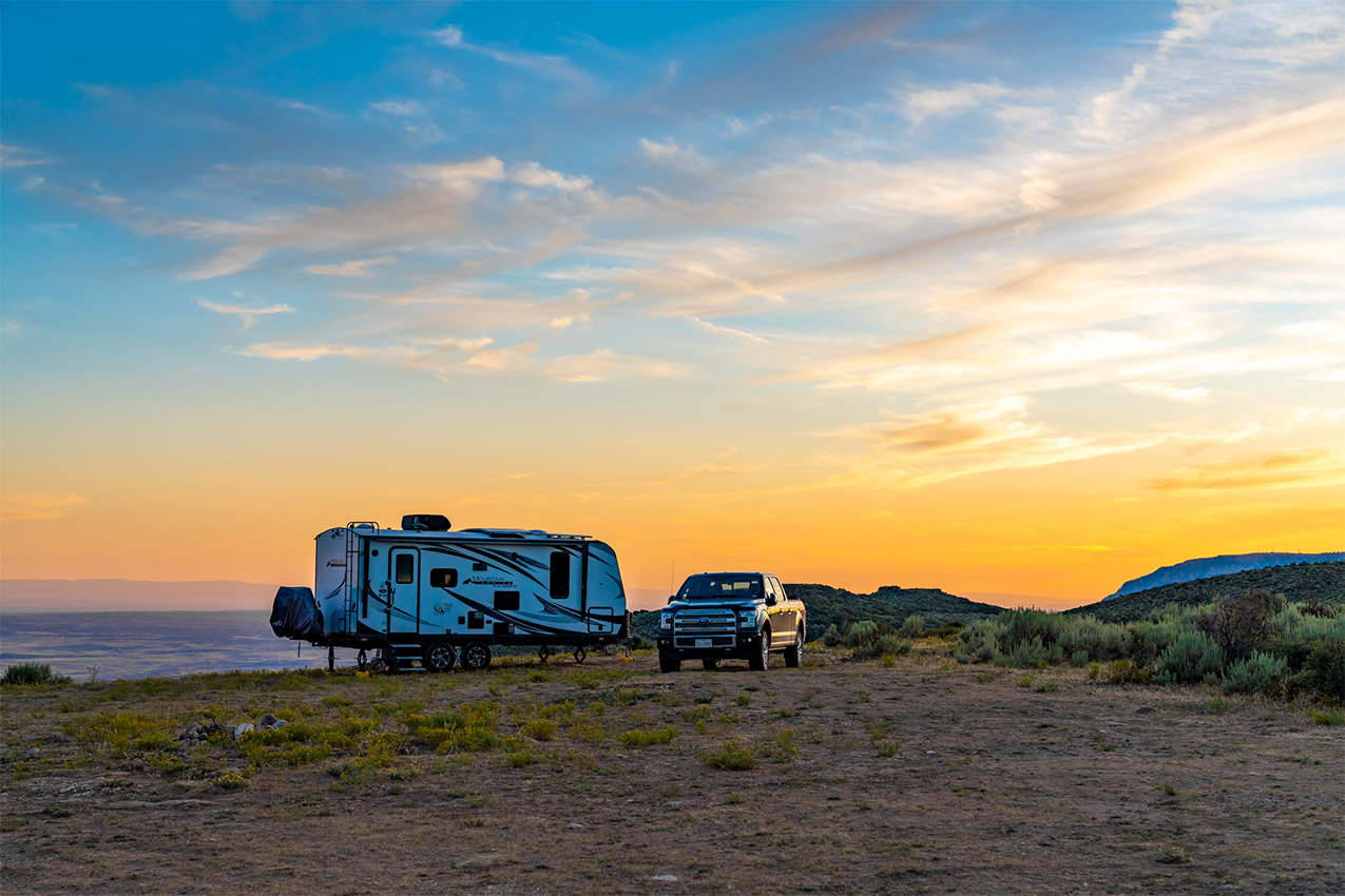 Truck and travel trailer camped on a plateau at sunset.
