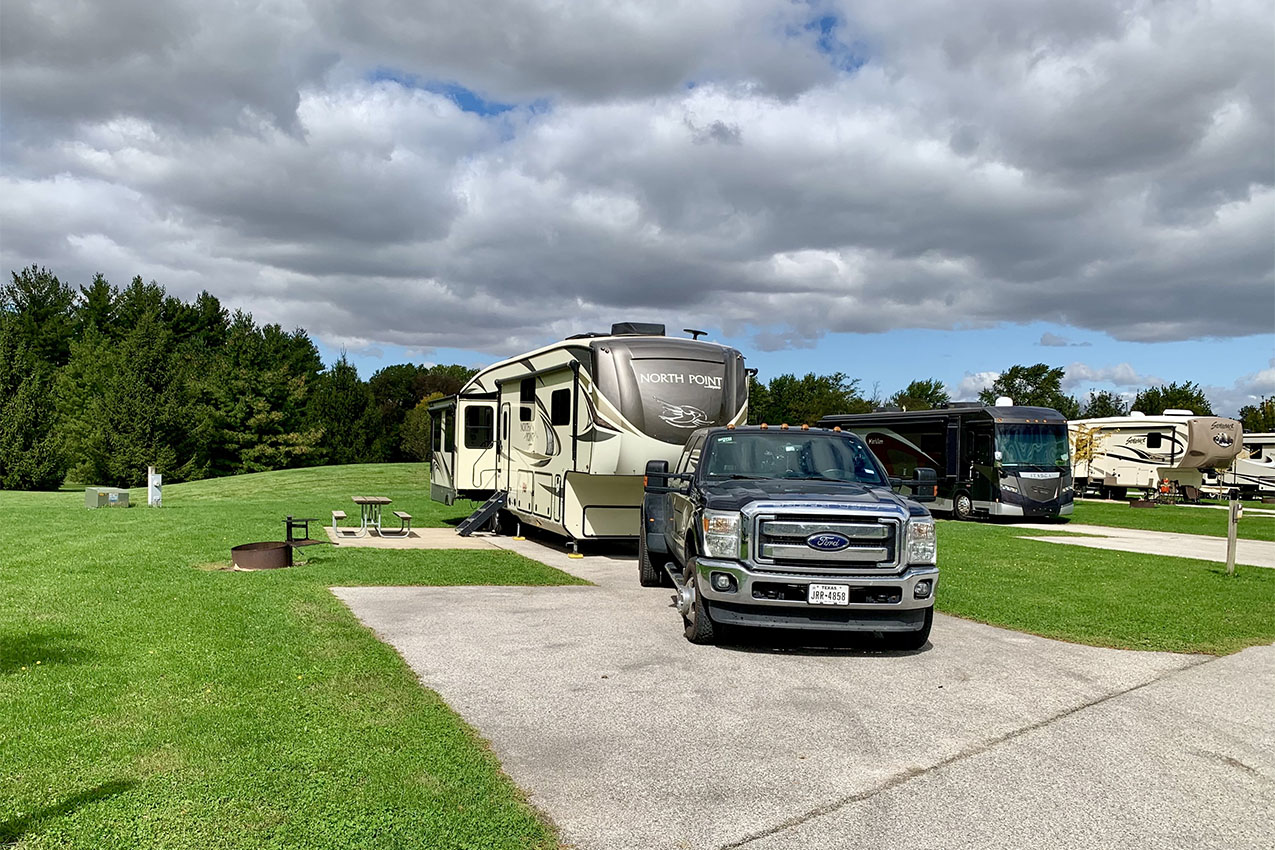 Large fifth wheel and truck parked on a paved site in a big grass field.